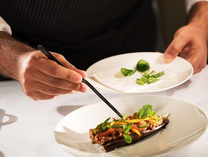 Stelle Michelin - nella foto uno chef di cui si vedono solo le mani sta posizionando delle foglioline versi su un piatto bianco che contiene del cibo e con l altra mano tiene un piatto bianco con foglioline verdi