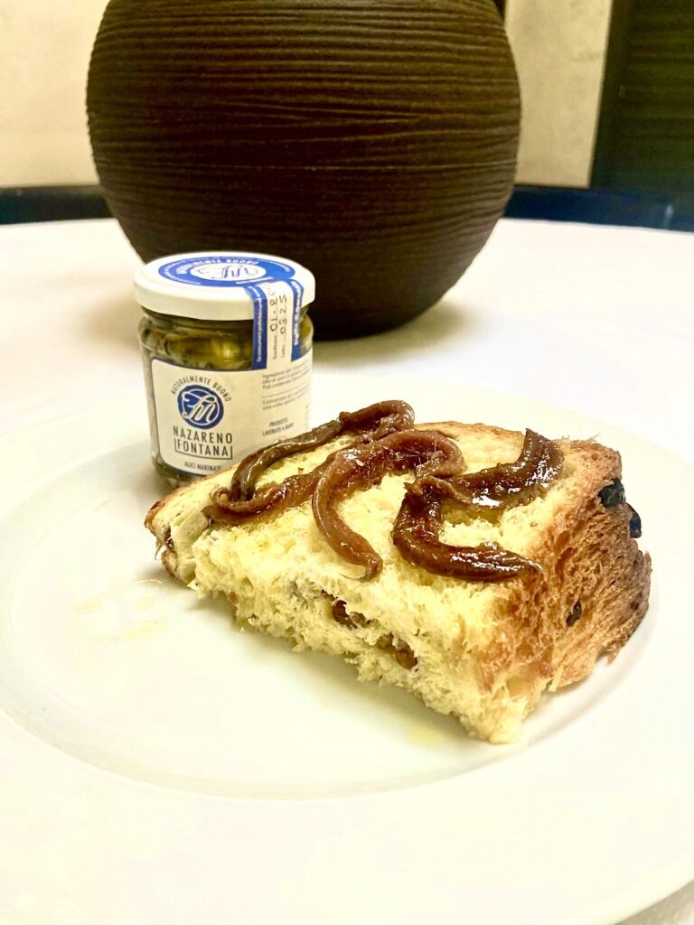 Un afetta di panettone con sopra alici marinate, affianco un vasetto di vetro con la salsa di alici