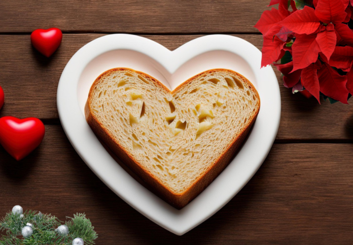 Il pane a forma di cuore dentro un piatto bianco a forma di cuore, appoggiato su un tavolo di legno e intorno ci sono dei fiori rossi di stella di Natale e dei cuoricini rossi e in basso a sinistra del biancospino verde