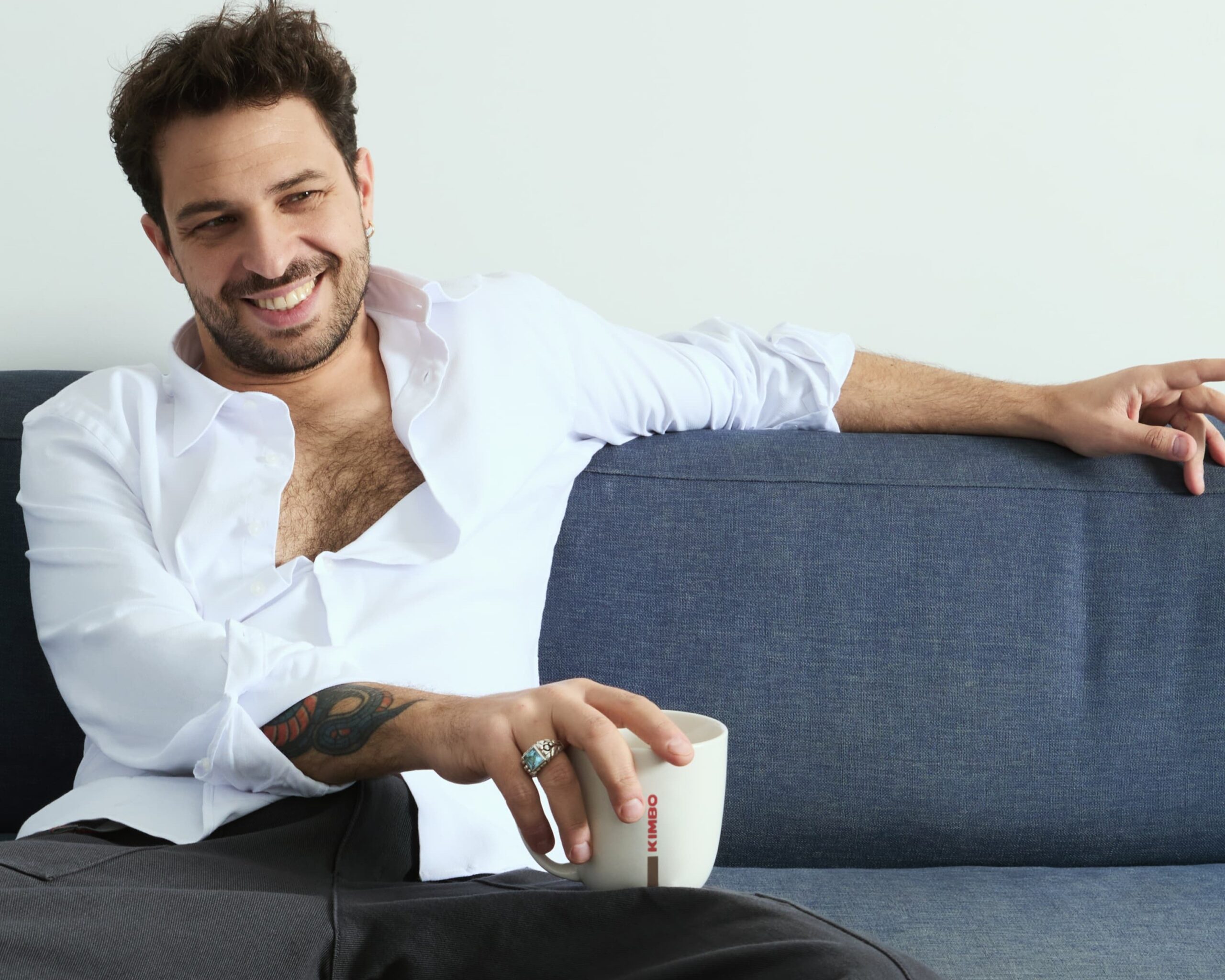 walter ricci, camicia biaanca e pantaloni scuri, è seduto su un divano e tiene nella mano destra una tazza