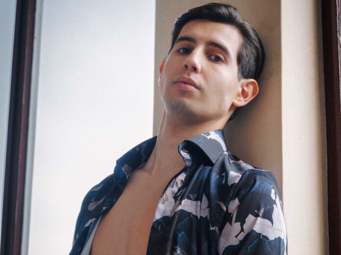 paolo martini in primo piano, appoggiato a una parete, indossa una camicia a quadri, sbottonata sul petto