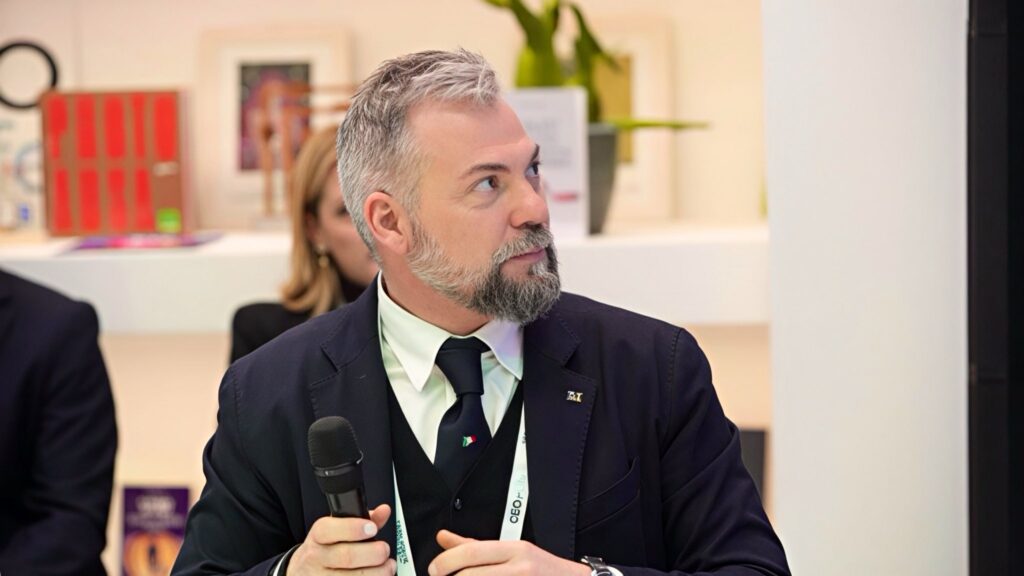 Giornata Nazionale Arandora Star - Foto di profilo e con il microfono in mano dell'onorevole Enzo Amich che indossa giacca scura, camicia bianca, cravatta scura. Porta capelli corti brizzolati barba baffi e pizzetto