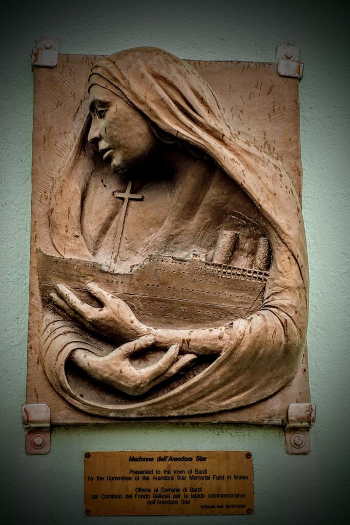 Bassorilievo in bronzo, con la Madonna ammantata, di profilo, che abbraccia la nave.