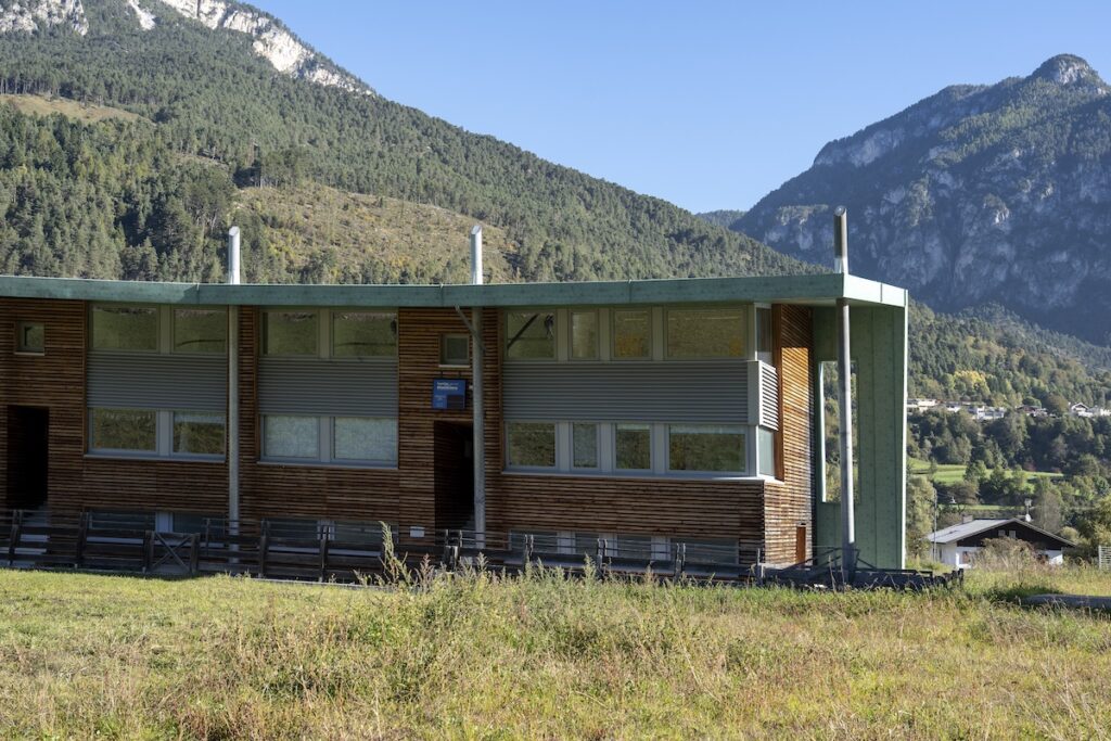 legno certificato - una struttura costruita prevalentemente in legno in mezzo a un prato con dietro le montagne