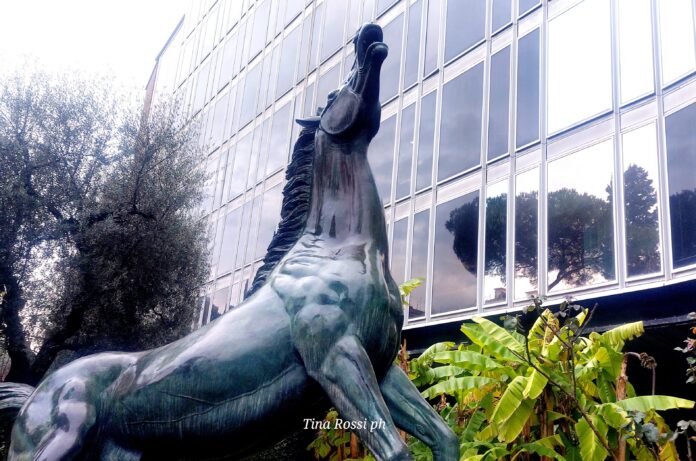 Programmi TV in prima serata - nella foto un enorme edificio a vetri e in primo piano la statua di bronzo di un cavallo