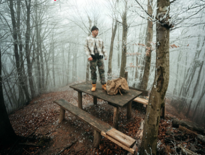 Biguan fuori il nuovo singolo Mi da me - Zetatielle Magazine biguan in piedi su un tavolo di legno, dentro un bosco, indossa una tuta mimetica di stile militare
