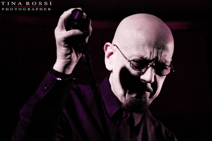 Canzonissima seconda puntata la dedica nella foto primo piano di Enrico Ruggweri sfondo nero occhiali da vista, testa rasata espressione cupa