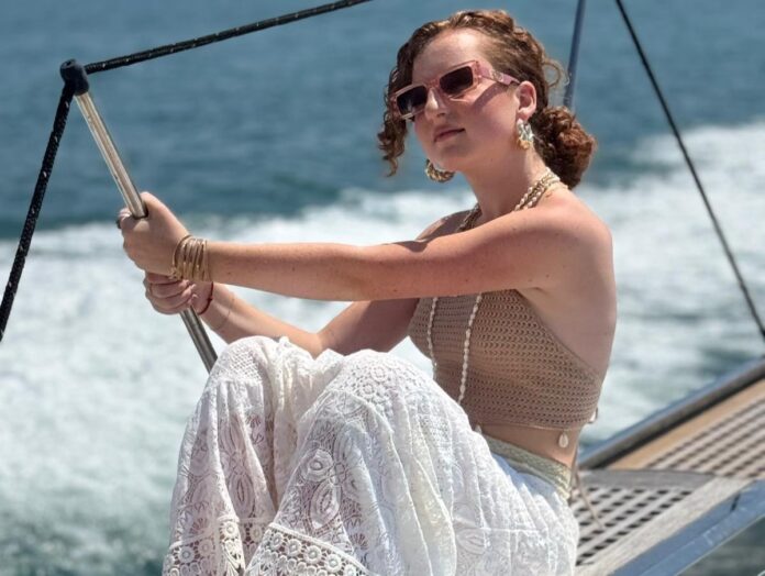 nicole in primo piano, vestita di chiaro, seduta sul ponte di uno yacht