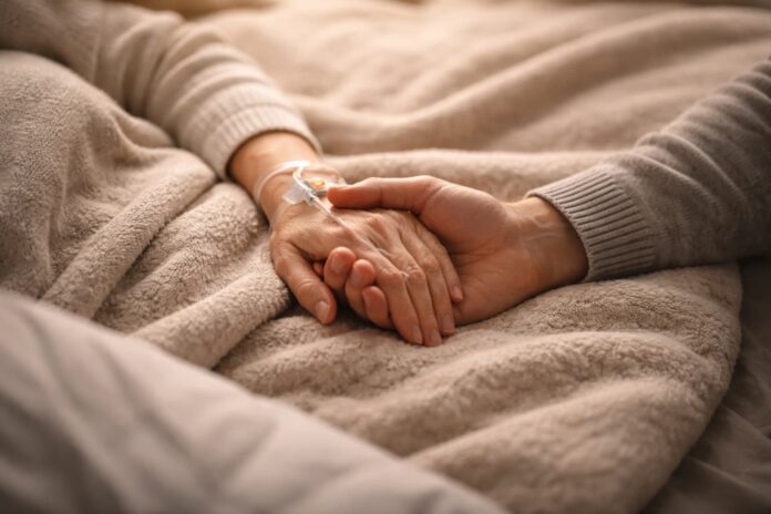 Il cancro e le sue storie di cuore - la mano di una donna nella mano di un uomo. La mano della donna ha una cnnnula infilata e si evince che sono in un letto, probabilmente di ospedale