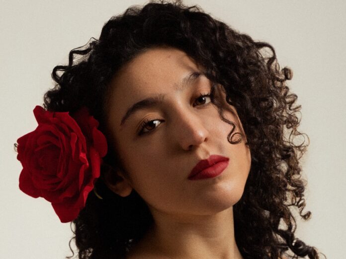 beatrice rosa in primo piano, ha una rosa rossa infilata nei capelli lunghi, neri e ricci