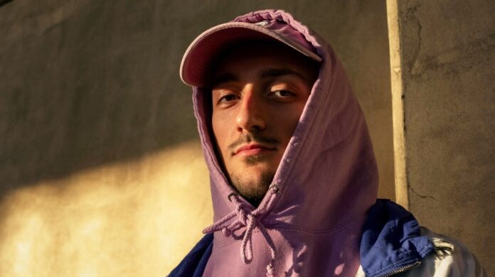 1 44 98 - il rapper in primo piano indossa una felpa violacea con il cappuccio calato sulla testa