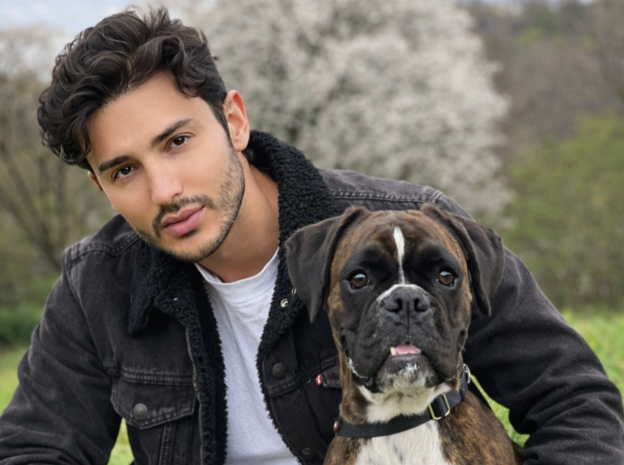 Andrea candeo con giubbotto scuro e maglietta bianca, capelli neri corti, abbraccia un cane marrone