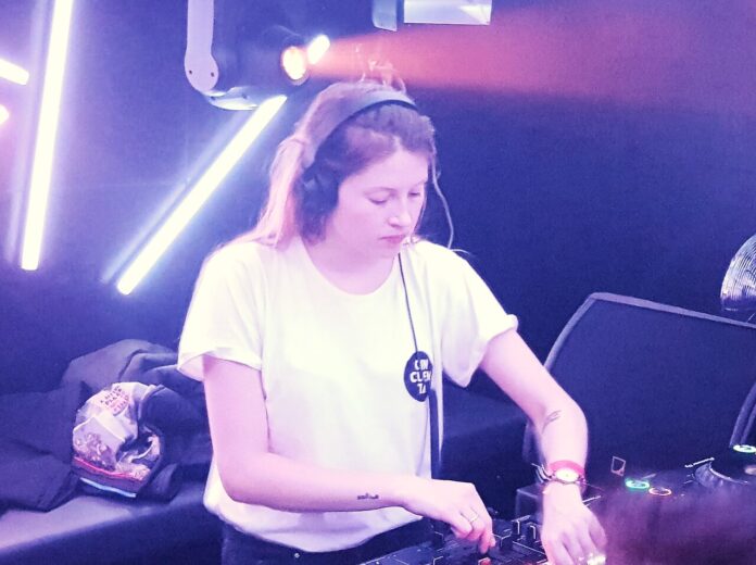 Charlotte de Witte - una donna con capelli lunghi biondi indossa un acuffia da dj, una t shirt bianca e sta lavorando alla consolle di una discoteca