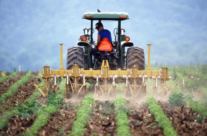 Sicurezza alimentare - nella foto un trattore con un uomo a bordo che lo guida, il trattore ha attaccato dietro uno spargitore di liquidi su un campo coltivato