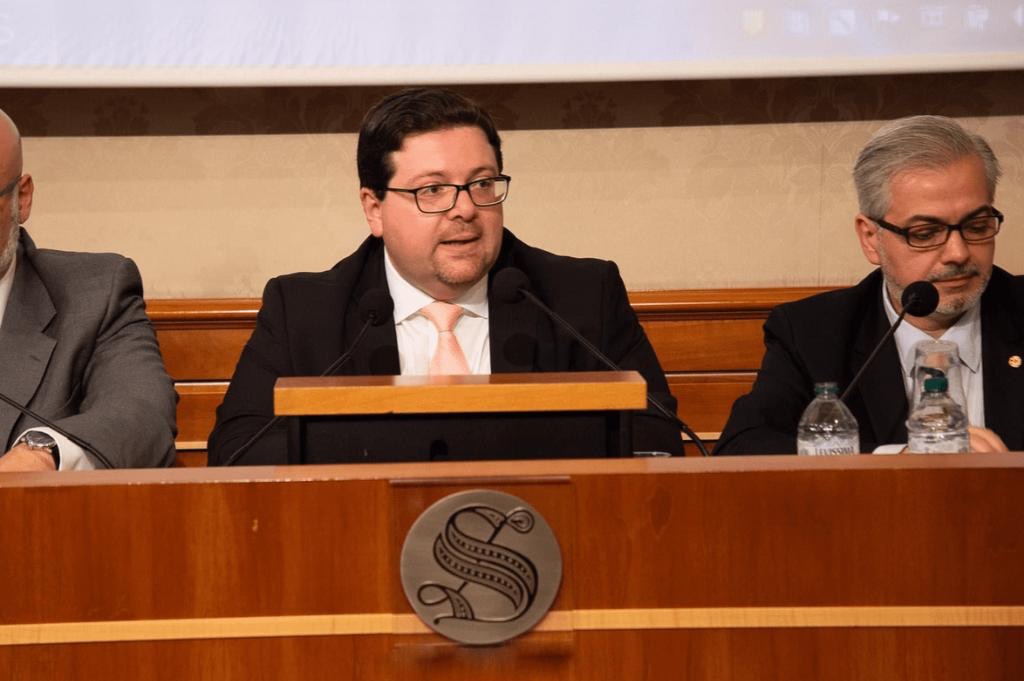 Cartolarizzazione sociale il Senato accoglie la proposta dell'U.C.I. - nella foto tre persone sedute al banco del Senato itlaiano, al centro l avv. Albanese sta parlando. Indossa occhiali da vista, giaccca scura, camicia bianca, porta capelli corti neri. Alla sua destra un altro uomo cxon giacca chiara e alla sua sinistra un altro uomo con giacca scura