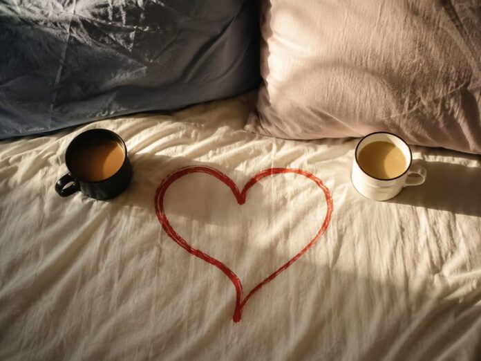 Italiani e il sesso sexting rapporto Censis - un letto disfatto con due coscini, un cuore rosso disegnato al centro tra due tazze di caffè - immagine genrata con IA