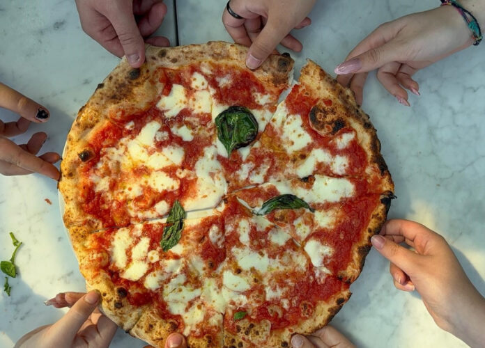 pizza therapy - una pizza vista dall'alto, con pomodoro mozzarella e basilico, tagliata a tranci e delle mani che si prendono le fette