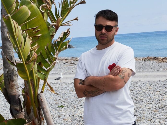 sorriso - diego pani in primo piano sulla spiaggia, di fianco a lui una palma