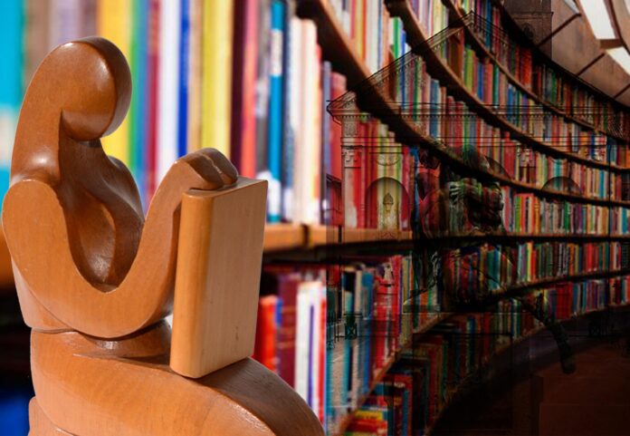 Mese della cultura Carmagnola - in primo piano una statua di legno rapppresentante una donna che legge seduta, la statua è vicina a una libreria ovale sulla quale è proiettata l'immagine di una chiesa con davanti un monumento di due persone
