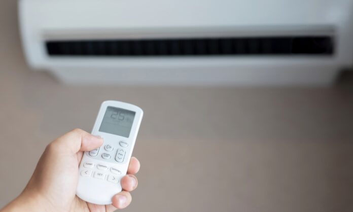Condizionatore bianco appeso alla parete e in primo piano una persona tiene in mano un telecomando impostato su 25