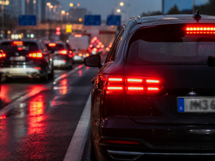 Frenata di emergenza cosa cambia con il nuovo Regolamento UE - ZETATIELLE MAGAZINE - IMMAGINE GENERATA CON IA FRENATA DI EMERGENZA - nella foto delle auto in coda su una strada, di notte, con la pioiggia, e in primo piano sulla destra il particolare di un auto con le luci rosse di frenata accese - immagine generata con IA